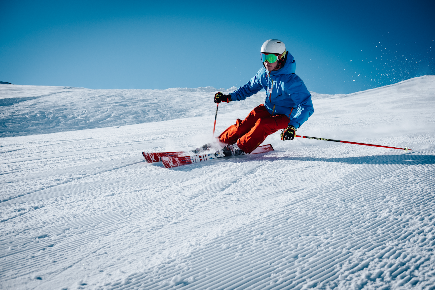 Close view of a skier carving freshly groomed snow under a blue sky.